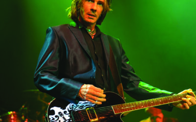 Musician Rick Springfield playing the guitar against a green background
